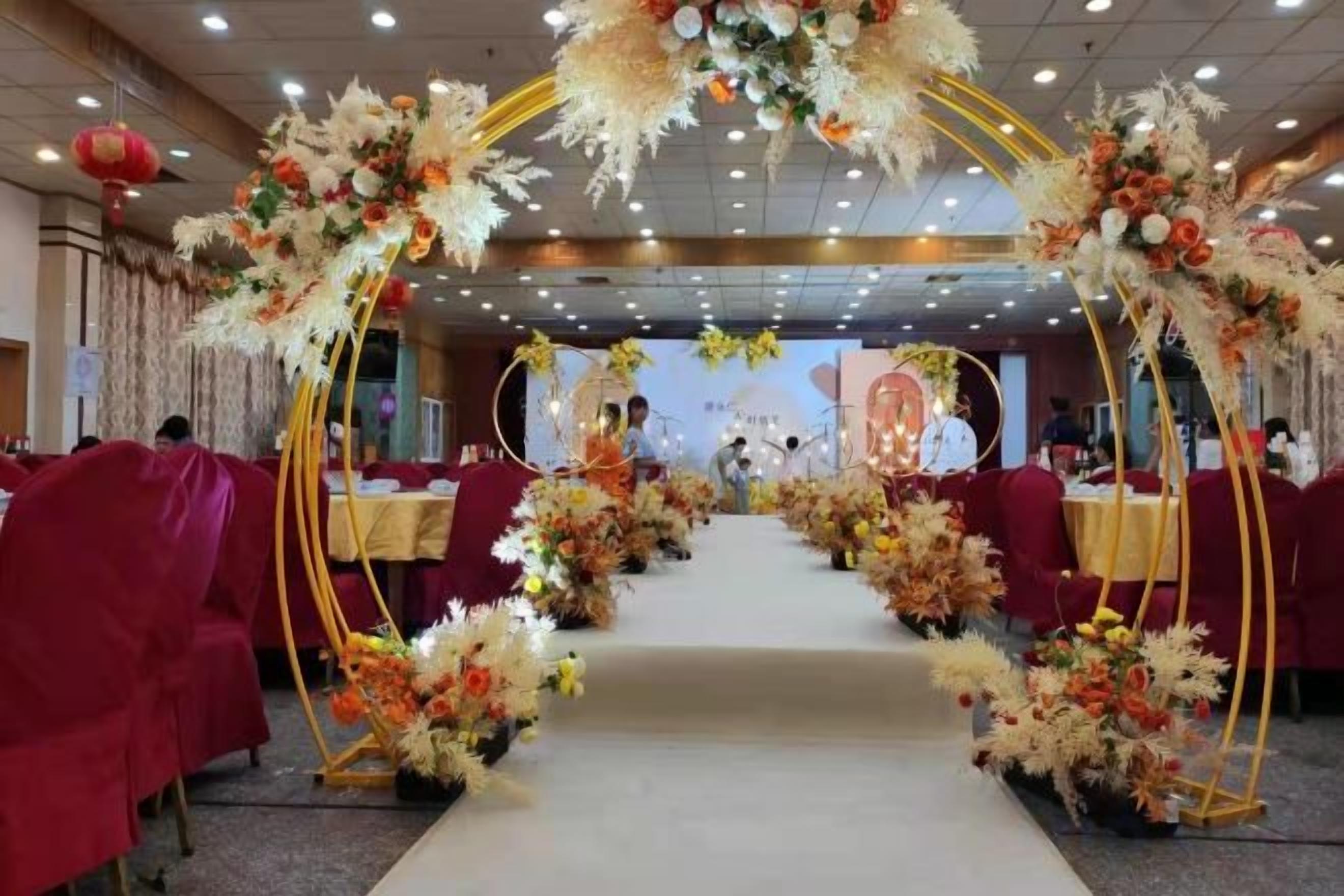 Een balzaal met aan tafelrijen gerangschikte tafels, een bloemrijke boog bij de ingang en een podium op de achtergrond.