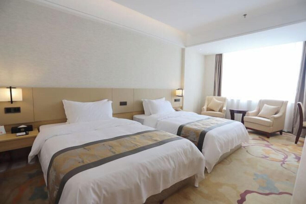 Une chambre d’hôtel avec deux lits, un canapé, une petite table et une grande fenêtre.