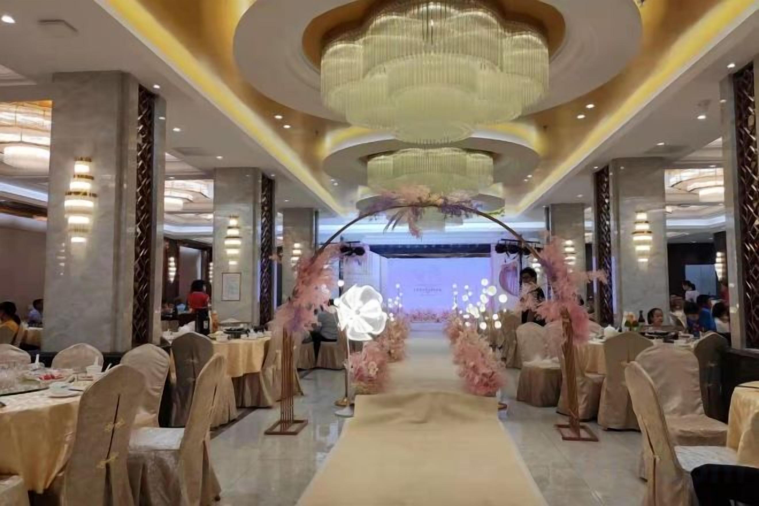A banquet hall with a central aisle, round tables, and a stage with floral decorations.