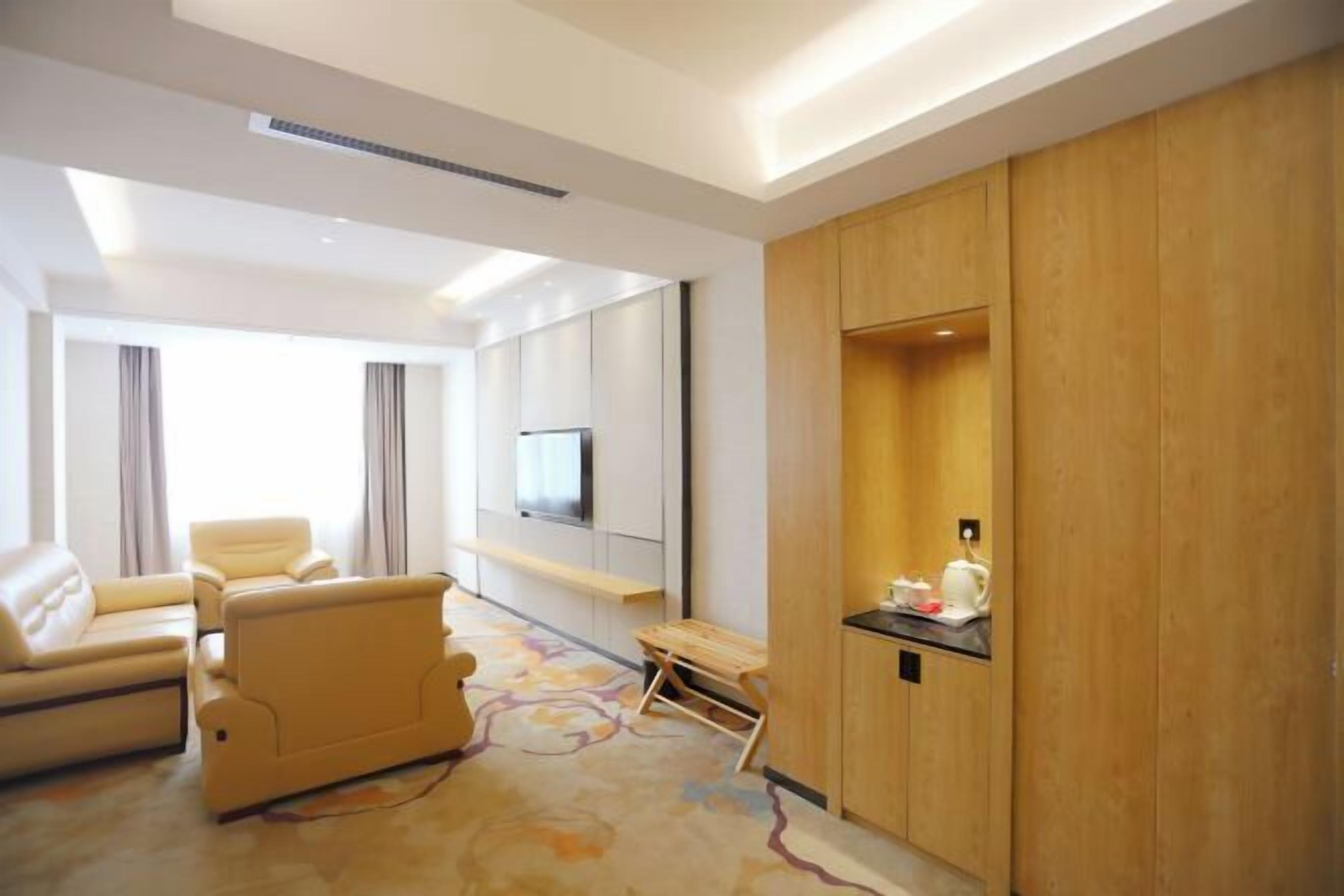Una habitación de hotel moderna con sofá, televisión montada en la pared, armario de madera y una mesita con tetera.