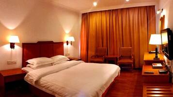 A hotel room with a large bed, two bedside lamps, a chair, a desk with a lamp, and a television.