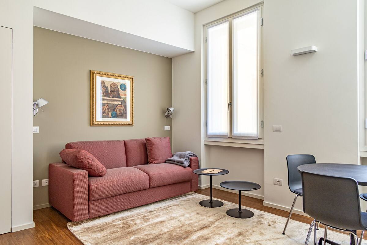 A living room with a red sofa, a small round table, and a framed picture on the wall.