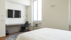 Et moderne soveværelse med en stor seng, et skrivebord med stol, et fjernsyn og et vindue.
