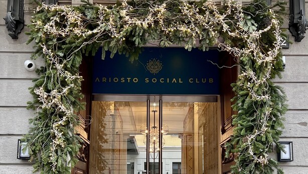 Indgangen til Ariosto Social Club med rød løber og dekorativt grøntværk.