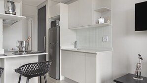A modern kitchen with white cabinetry, a stainless steel refrigerator, a sink, and a dining area with a black chair. - 707 at Two six two Florida Road (Durban)
