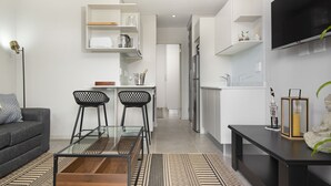 A modern living space with a sofa, a glass coffee table, a kitchen area with a fridge, and a TV mounted on the wall. - 707 at Two six two Florida Road (Durban)