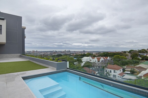 A rooftop pool with a city view, surrounded by greenery and residential buildings.