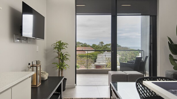 A modern living room with a flat-screen TV, a sofa, a dining table, and a balcony with a view of the city. - 707 at Two six two Florida Road (Durban)