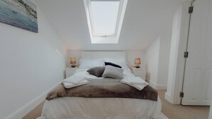 A bedroom with a skylight, a bed with white linens, two bedside tables with lamps, and a door to the right.