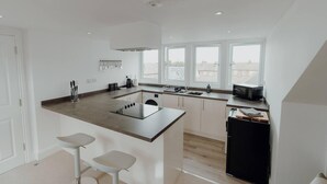 A modern kitchen with a central island, bar stools, a black refrigerator, and a window overlooking a residential area.