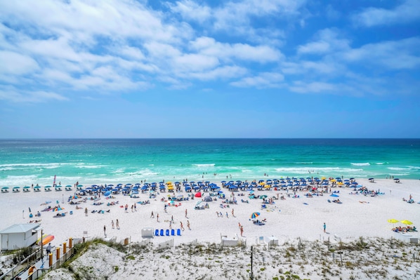 Ein Strand mit vielen Sonnenschirmen und Liegestühlen, ein sandiger Uferstreifen und das Meer.