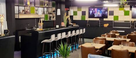 Zona de bar moderna con mostrador, taburetes y una pantalla de televisión. Hay mesas y sillas dispuestas para comer.