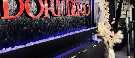 Un área de recepción con un letrero iluminado grande que dice 'DORMIERO' y una pared decorativa con una fuente de agua.