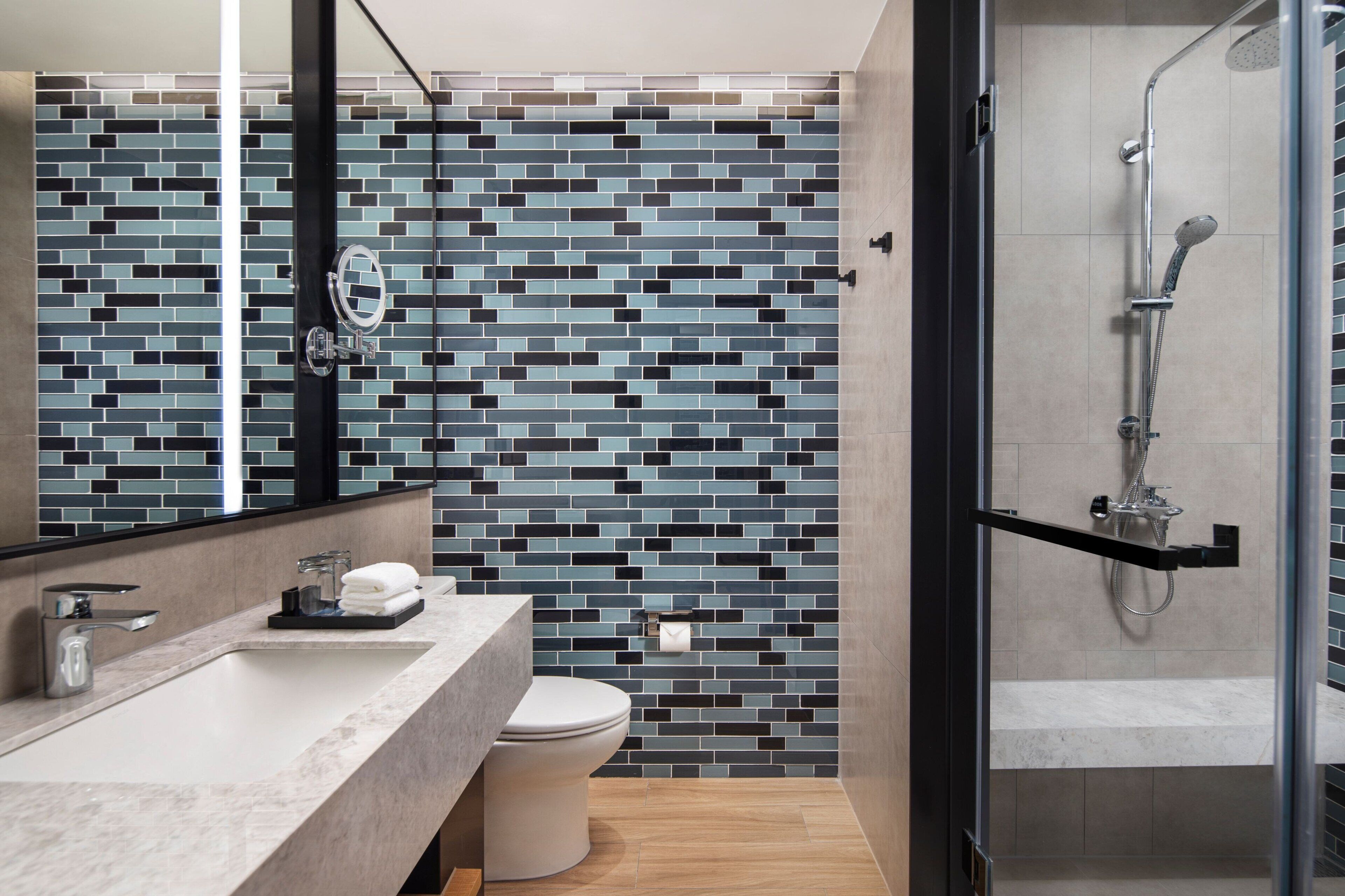 A modern bathroom with a tiled backsplash, a glass shower enclosure, and a marble sink.
