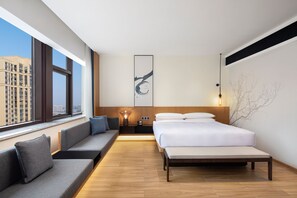 A modern hotel room with a large bed, a sofa, a bedside table, and a view of the city through large windows. - Fairfield By Marriott Hangzhou Xiaoshan (Hangzhou)