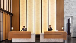 A reception area with two wooden reception desks, a marble floor, and a patterned wall in the background. - Fairfield By Marriott Hangzhou Xiaoshan (Hangzhou)