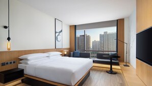 A modern hotel room with a large bed, a seating area, a TV, and a view of the cityscape. - Fairfield By Marriott Hangzhou Xiaoshan (Hangzhou)