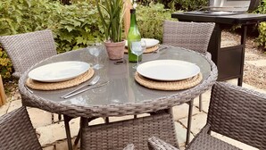 A round outdoor table with two plates, cutlery, and a glass of water, surrounded by wicker chairs. - Come & Stay on a Real Norfolk Vineyard (Norwich)