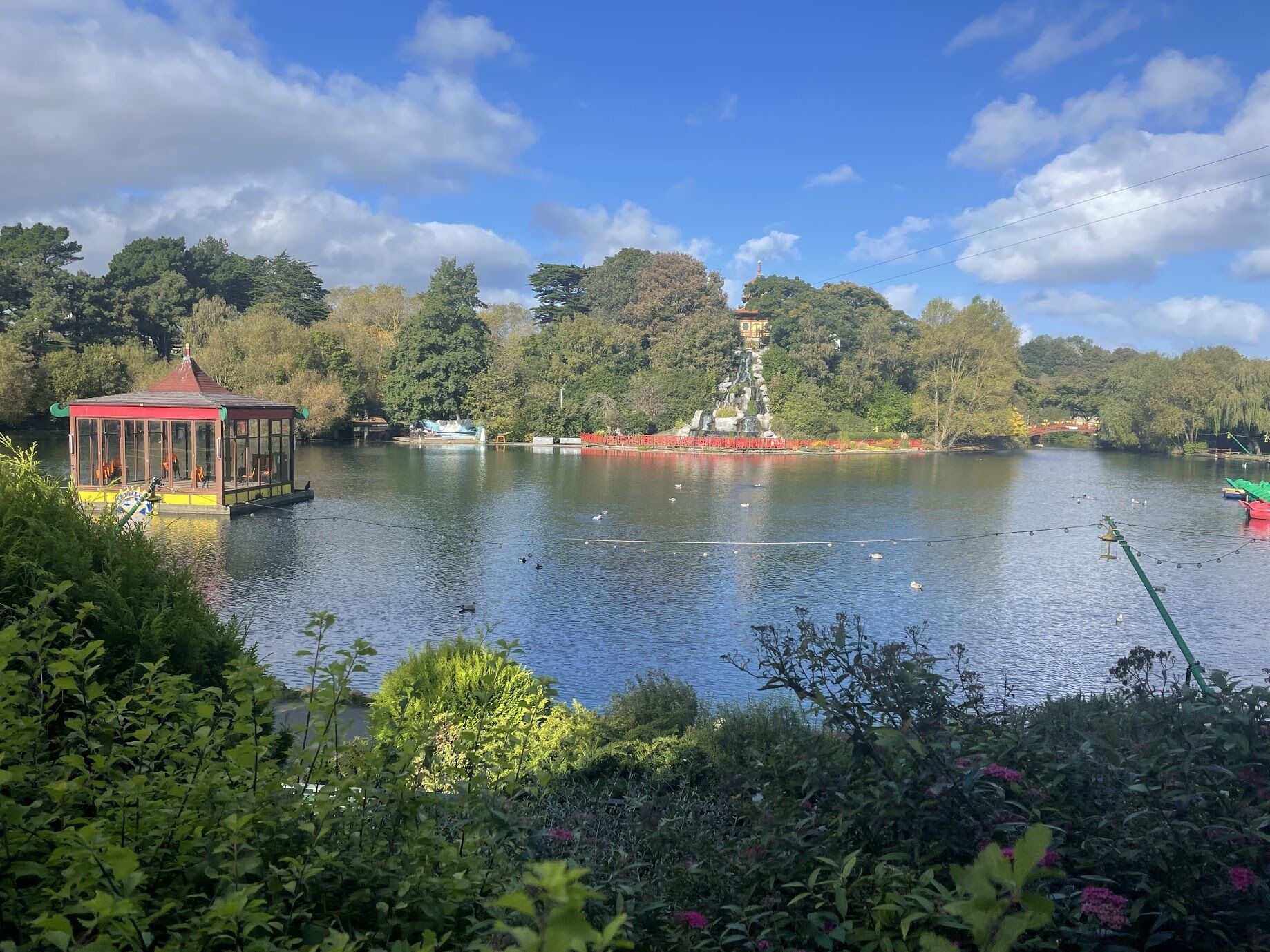 A serene lakeside scene with a pavilion, a pagoda-like structure, and lush greenery.