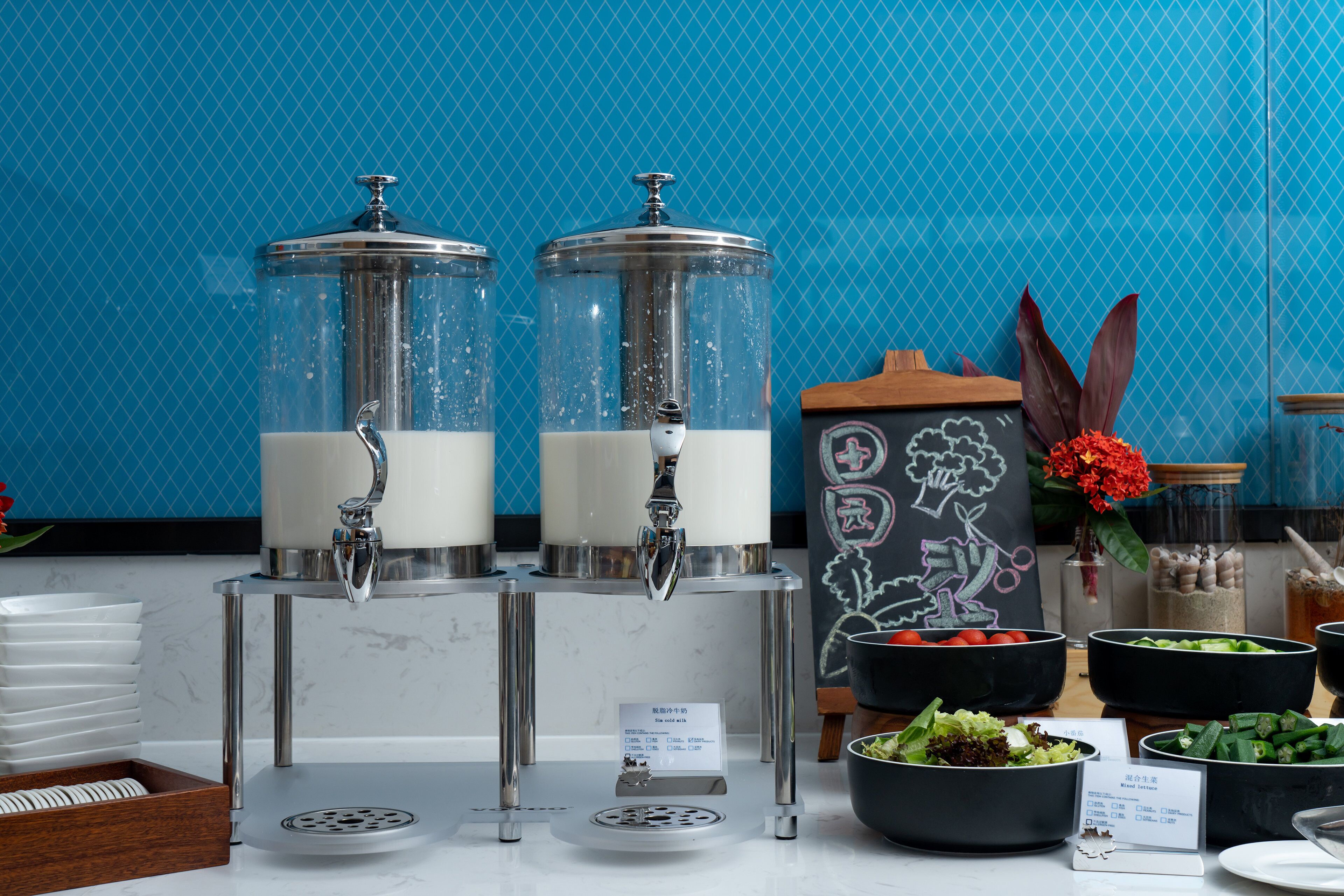 A buffet setup with two beverage dispensers, various food bowls, and a chalkboard with drawings.