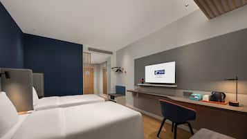 A modern hotel room with two beds, a desk, a chair, a TV, and a small kitchenette.