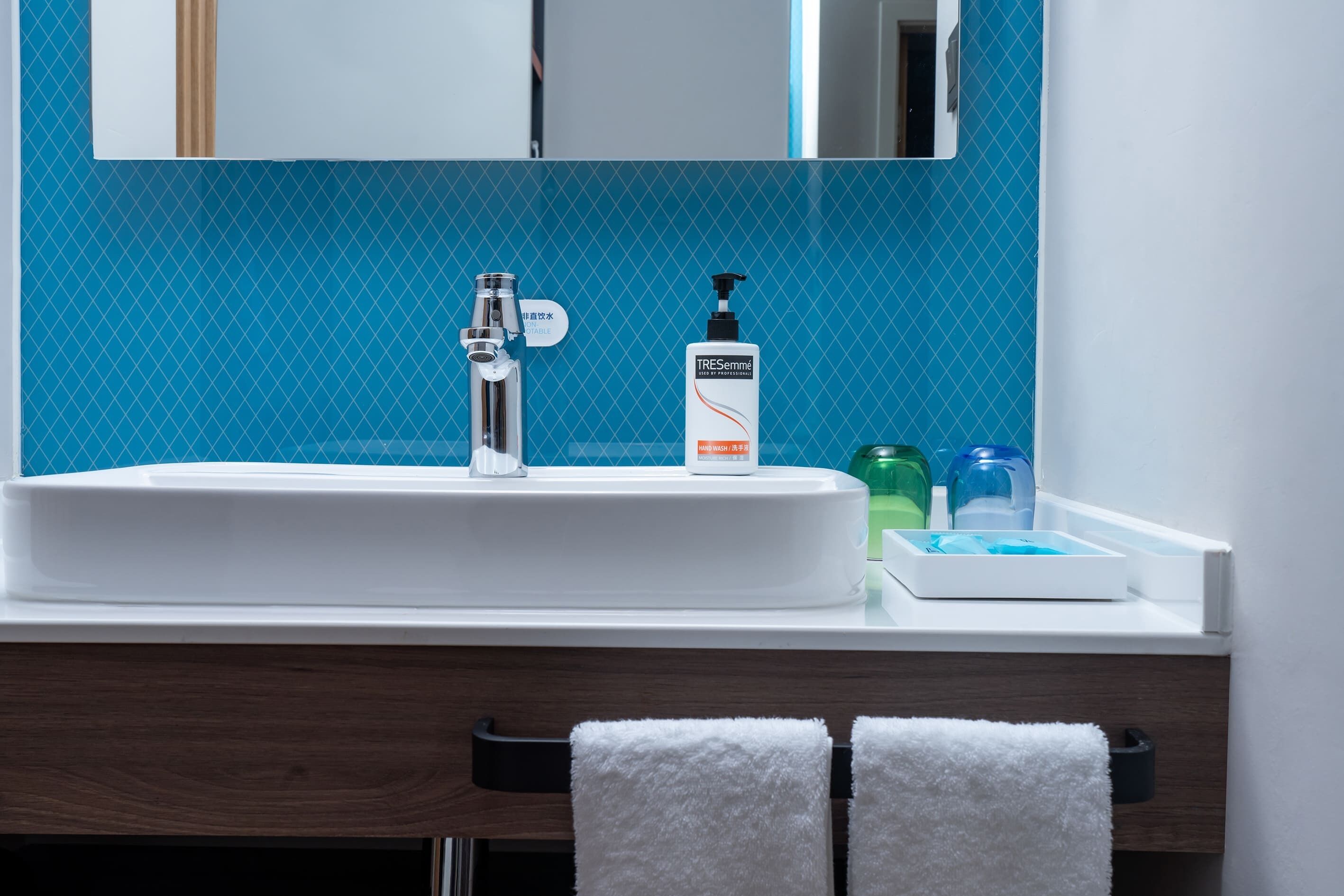 A bathroom with a white sink, a mirror, and a blue tiled wall.