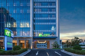 A Holiday Inn Express hotel with a modern glass facade, a well-lit entrance, and a landscaped area with palm trees. - Holiday Inn Express Beihai Silver Beach by IHG (Beihai)