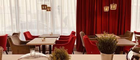 Interior de restaurante con mesas, sillas y un telón rojo de fondo.