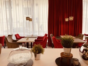 Interior de restaurante con mesas, sillas y un telón rojo de fondo.
