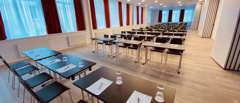 A conference room with rows of tables and chairs, large windows with red curtains, and a modern ceiling design.