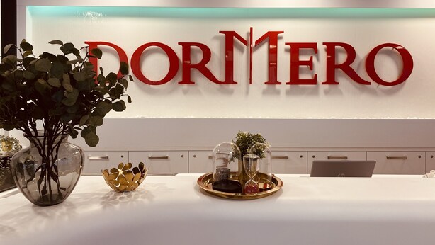 Un área de recepción con un gran letrero de 'DORMERO', un mostrador de recepción blanco y una bandeja decorativa con objetos.