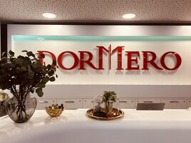 Un área de recepción con un gran letrero de 'DORMERO', un mostrador de recepción blanco y una bandeja decorativa con objetos.