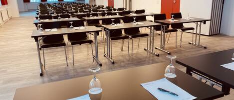 Un salón de conferencias con filas de mesas, cada una con un bolígrafo y un vaso de agua.