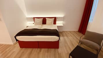 Un dormitorio moderno con una cama, mesitas de noche, una silla y una ventana con cortinas.