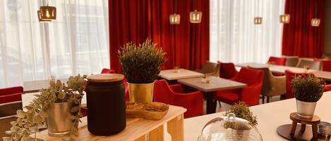 A restaurant interior with red curtains, wooden tables, and potted plants.