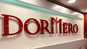 Una pared con el nombre 'DORMERO' en letras rojas grandes, un borde de piedras blancas y un techo moderno con paneles perforados.