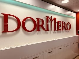 Una pared con el nombre 'DORMERO' en letras rojas grandes, un borde de piedras blancas y un techo moderno con paneles perforados.