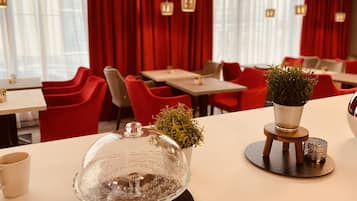 A restaurant interior with red chairs, tables, and a potted plant on a table.