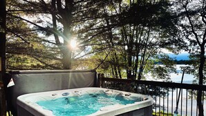 A hot tub on a wooden deck with a view of a lake and trees.