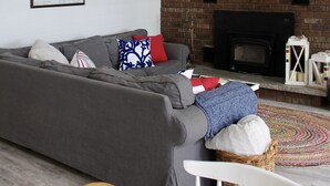 A living room with a gray sofa, a wooden table, a fireplace, and a flat-screen TV mounted above the fireplace.
