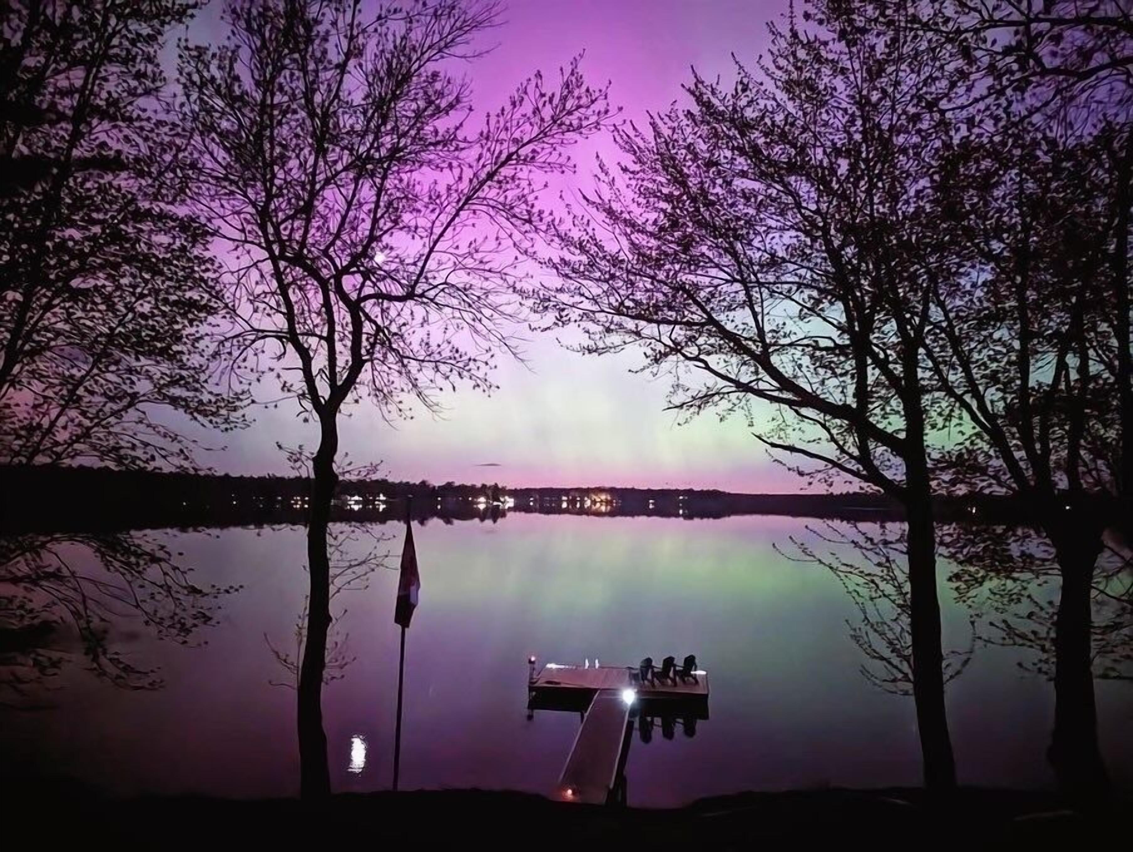 A dock extending into a calm lake with a clear reflection of the sky, surrounded by trees.