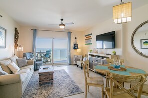 Relax in a spacious living area with a sofa, dining table, and ceiling fan, offering a view of the outdoors and a flat-screen TV for entertainment.