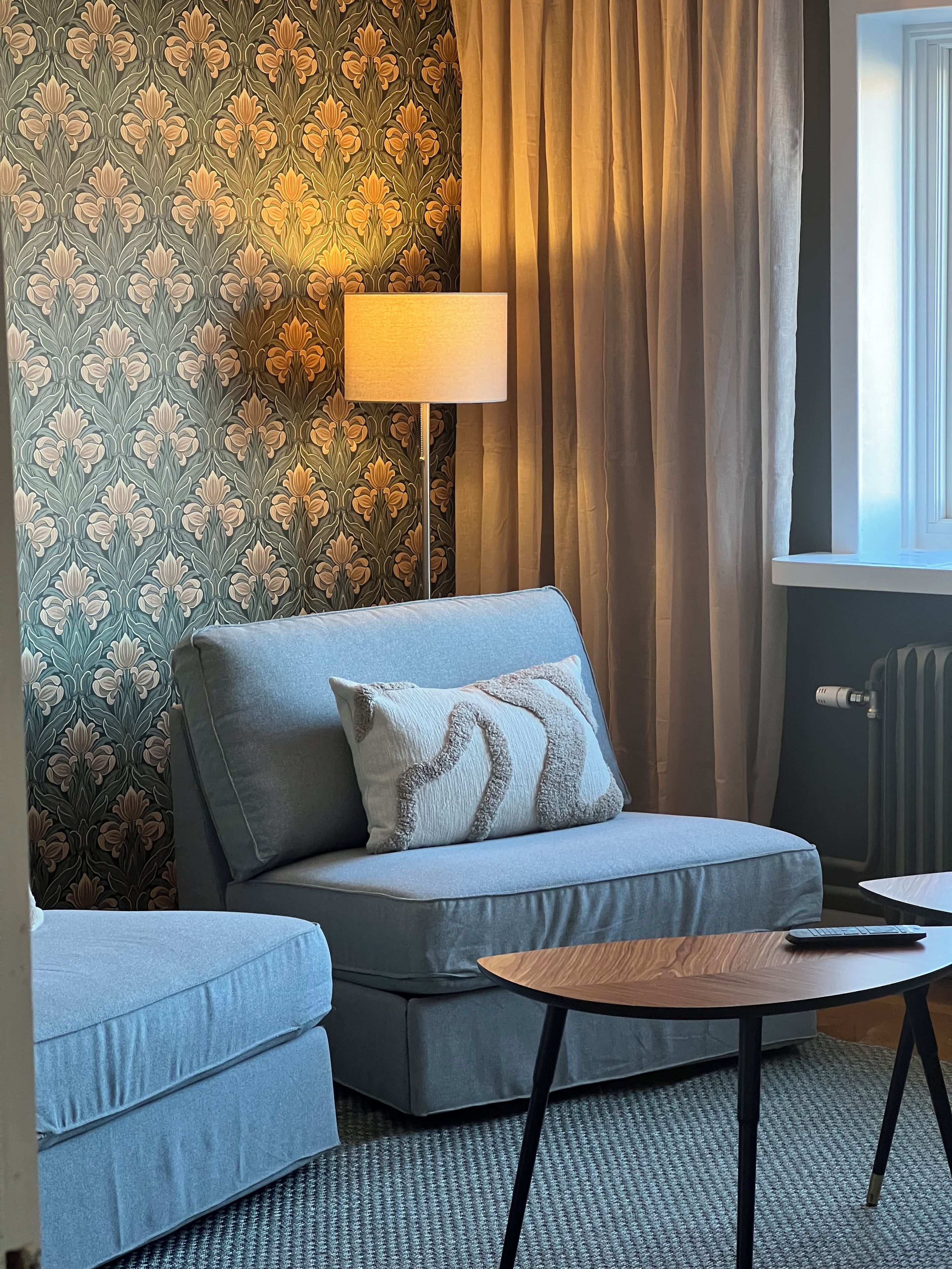 Ein Zimmer mit einer Couch, einem kleinen Tisch, einer Lampe und einer Heizung.