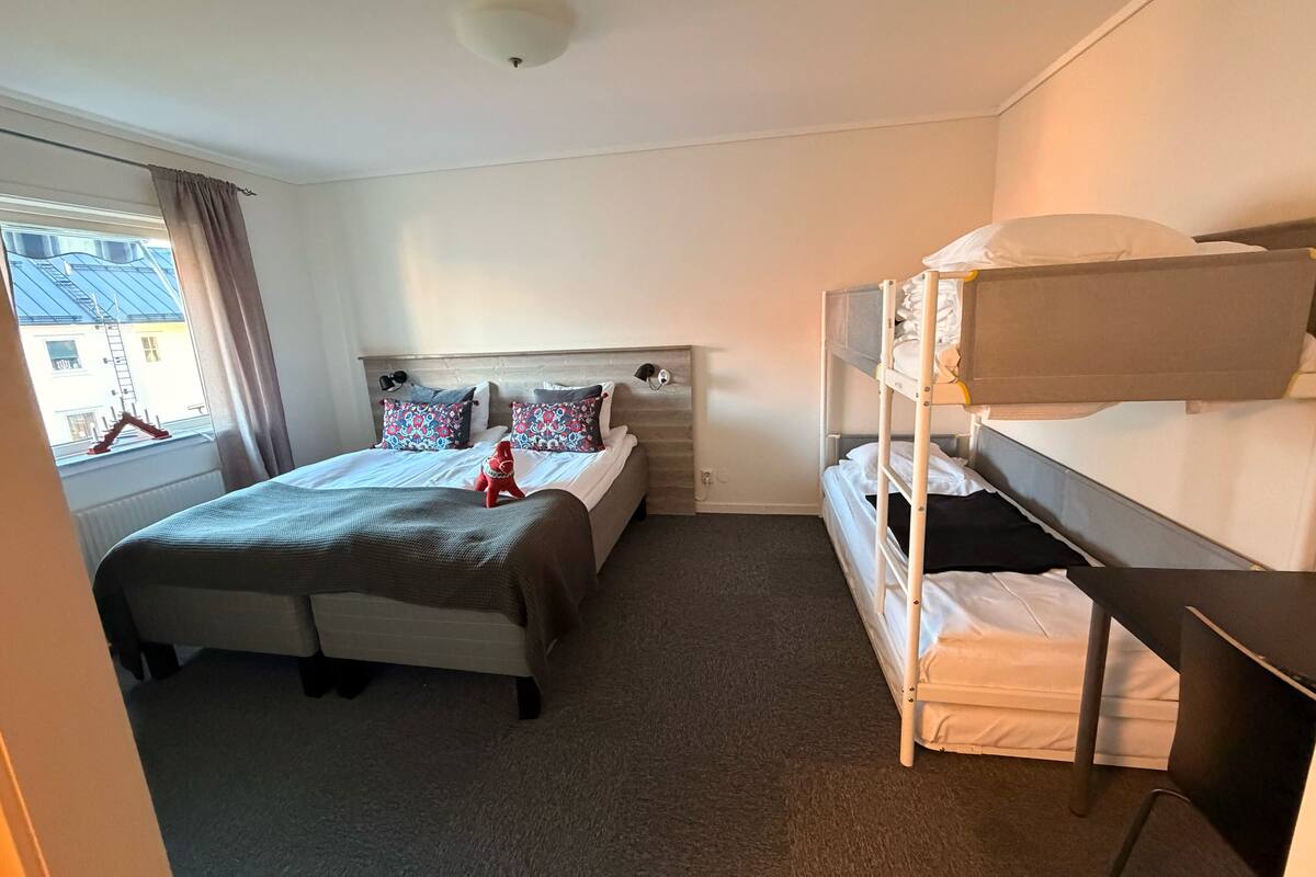 Una cama individual con cabecera, una cama litera, una ventana con cortinas y un radiador.