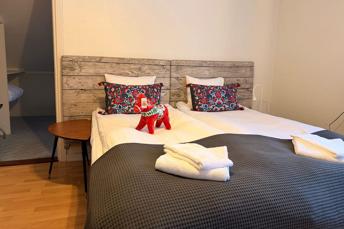 Una cama bien hecha con un cabecero estampado, una mesita redonda y un cojín con forma de caballo rojo.