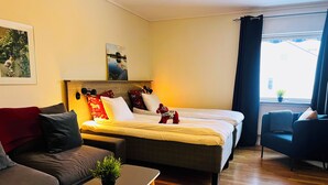 A modern hotel room with a bed, a sofa, a small table, and a view of the outdoors. - Fridhemsgatan City Stay (Mora)