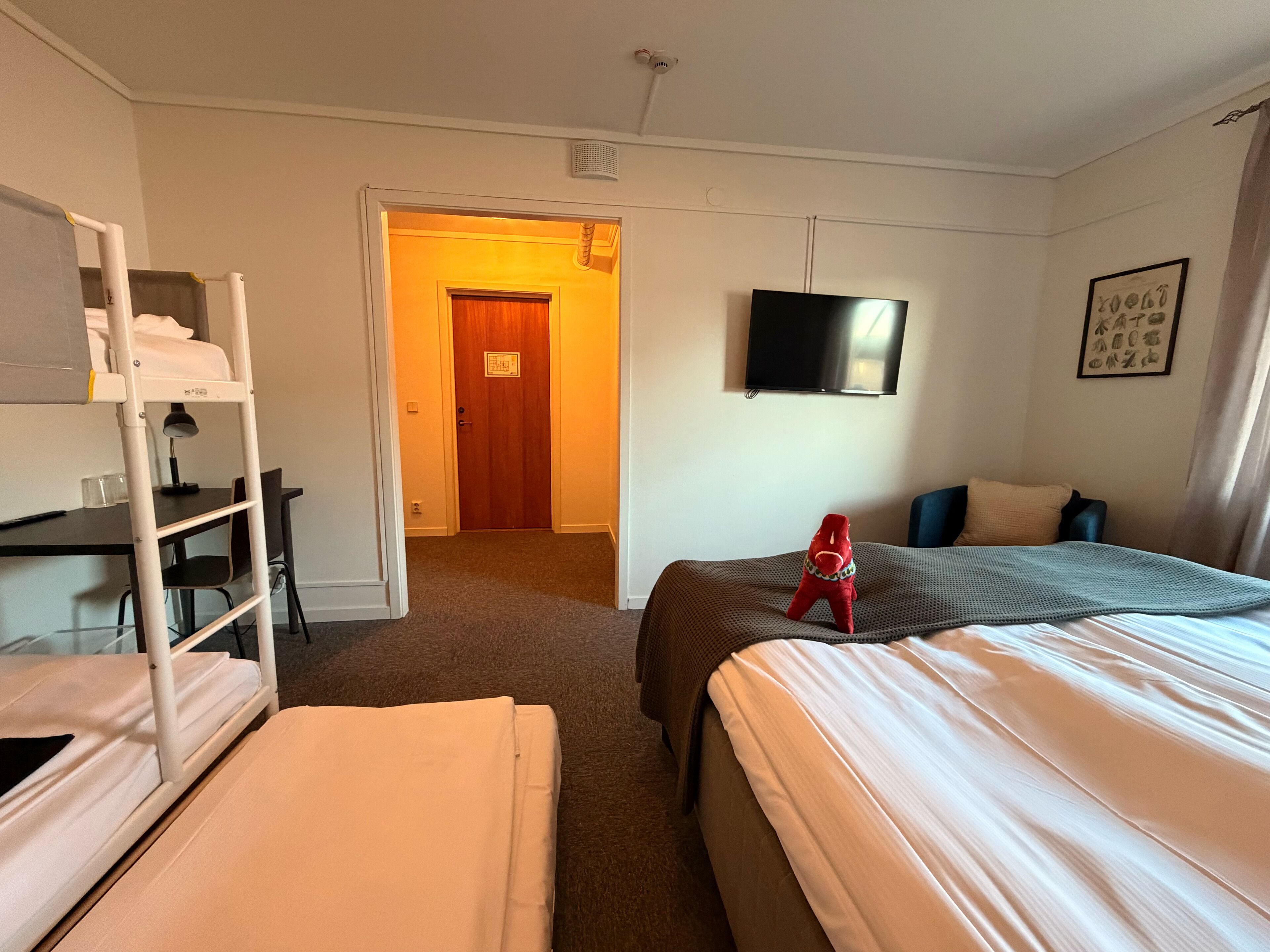 Habitación de hotel con dos camas, un escritorio, un televisor y una puerta que da a otra habitación.