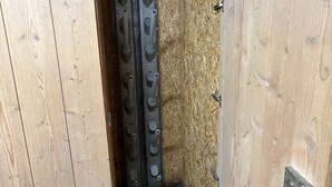 A wooden room with a metal door and a metal curtain rod.