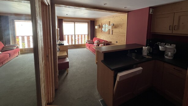 A room with a kitchenette, a sofa, a dining table, and a large window.