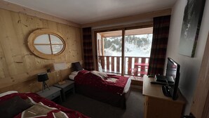 A room with two beds, a desk, a TV, and a window with a view of a snowy landscape.